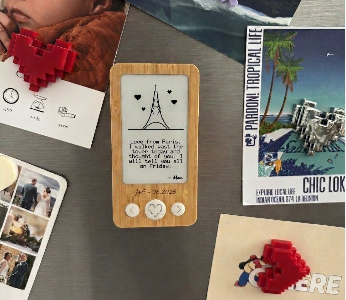Un cadre e-ink en bambou sur la porte du frigo, entre des photos et des cartes postales : on y voit un dessin et un mot